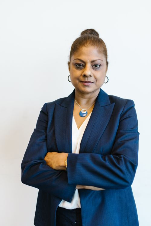 A woman in a navy blazer standing square to the camera with her arms crossed and a composed expression