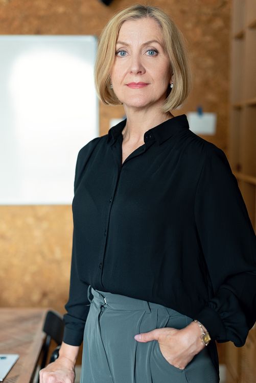 A woman in a black shirt and gray trousers standing at an angle with one hand in her pocket