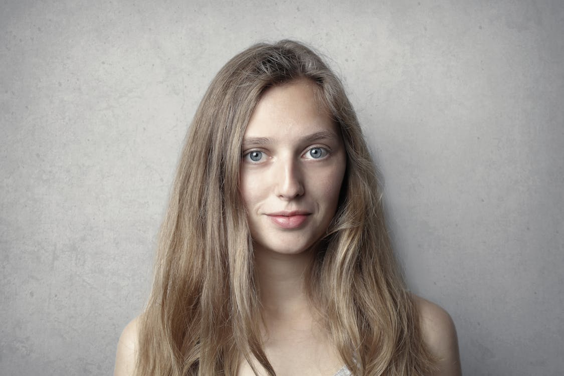 Woman with long light brown hair in front of a plain light gray textured wall