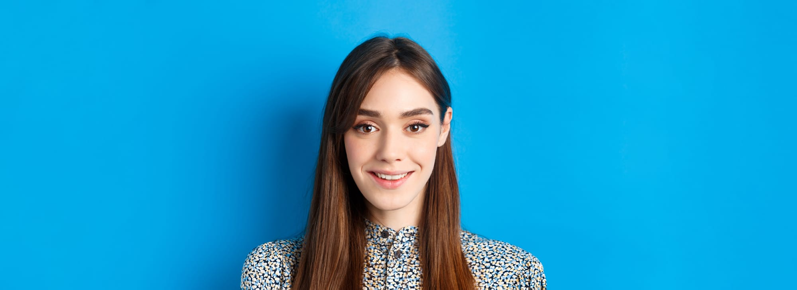 Woman with long brown hair smiling in front of a solid bright blue headshot background