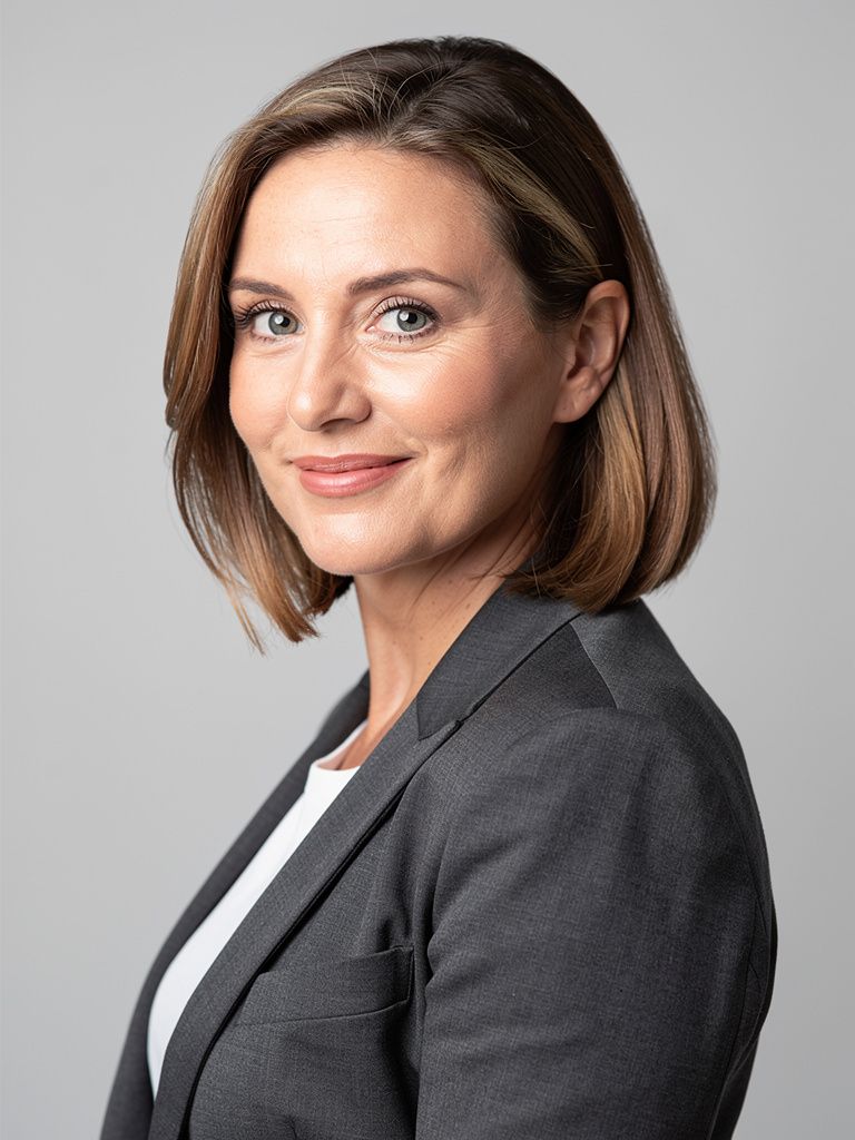 A woman in her forties in a charcoal blazer in a three-quarter turn with her face back to the camera